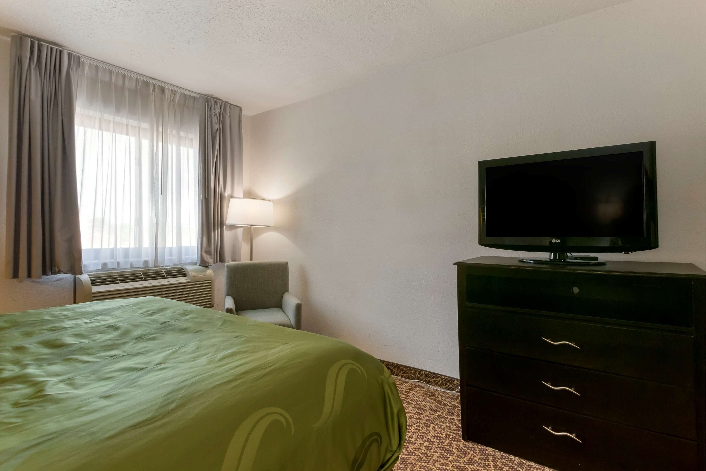 Una habitación de hotel con una cama, un televisor en una cómoda, una silla y una ventana con cortinas.