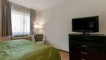 Una habitación de hotel con una cama, un televisor en una cómoda, una silla y una ventana con cortinas.