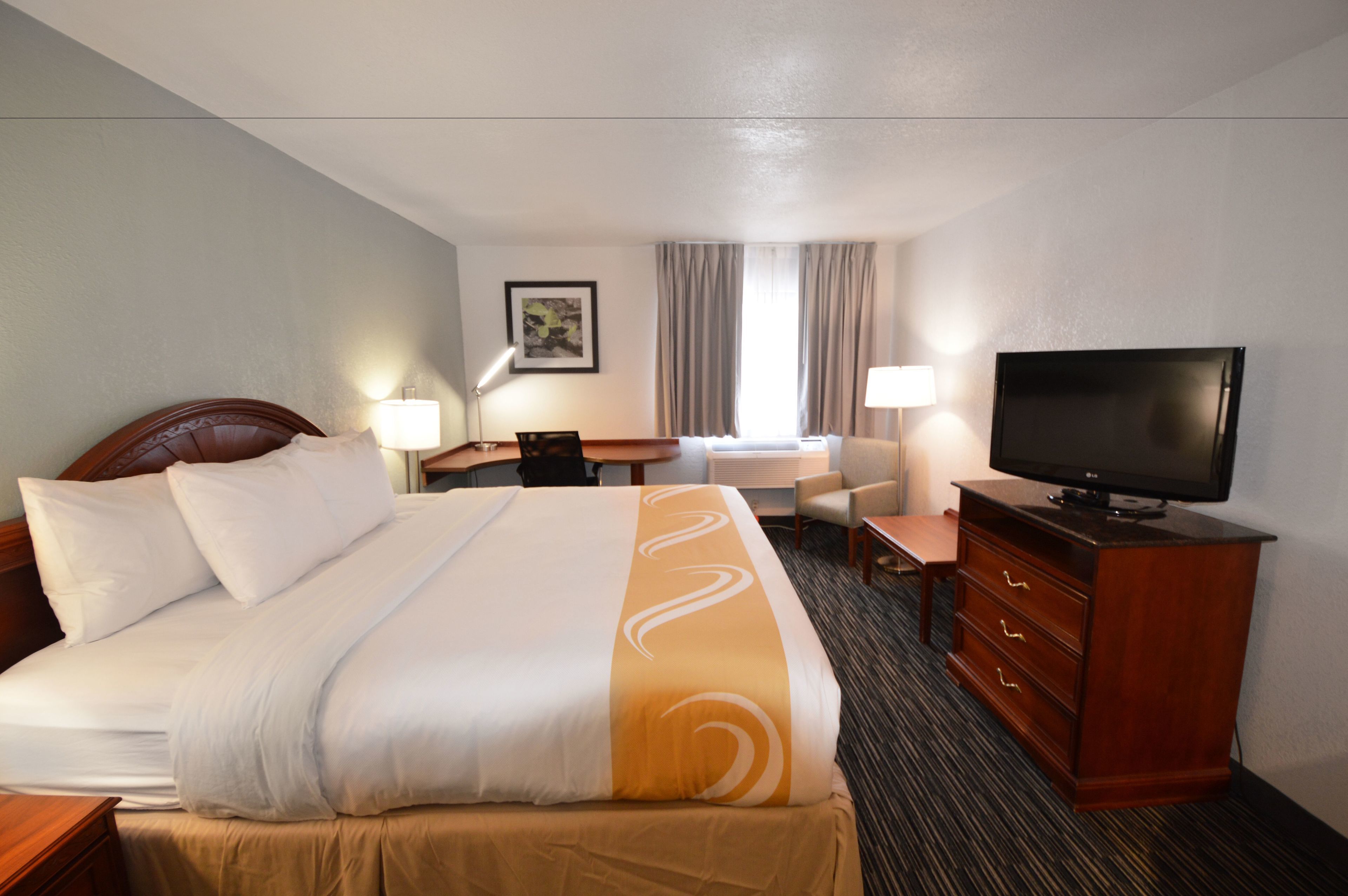 A hotel room with a large bed, a television, a desk, and a chair.