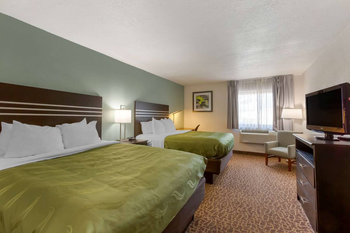 A hotel room with two beds, a TV, a desk, and a chair.