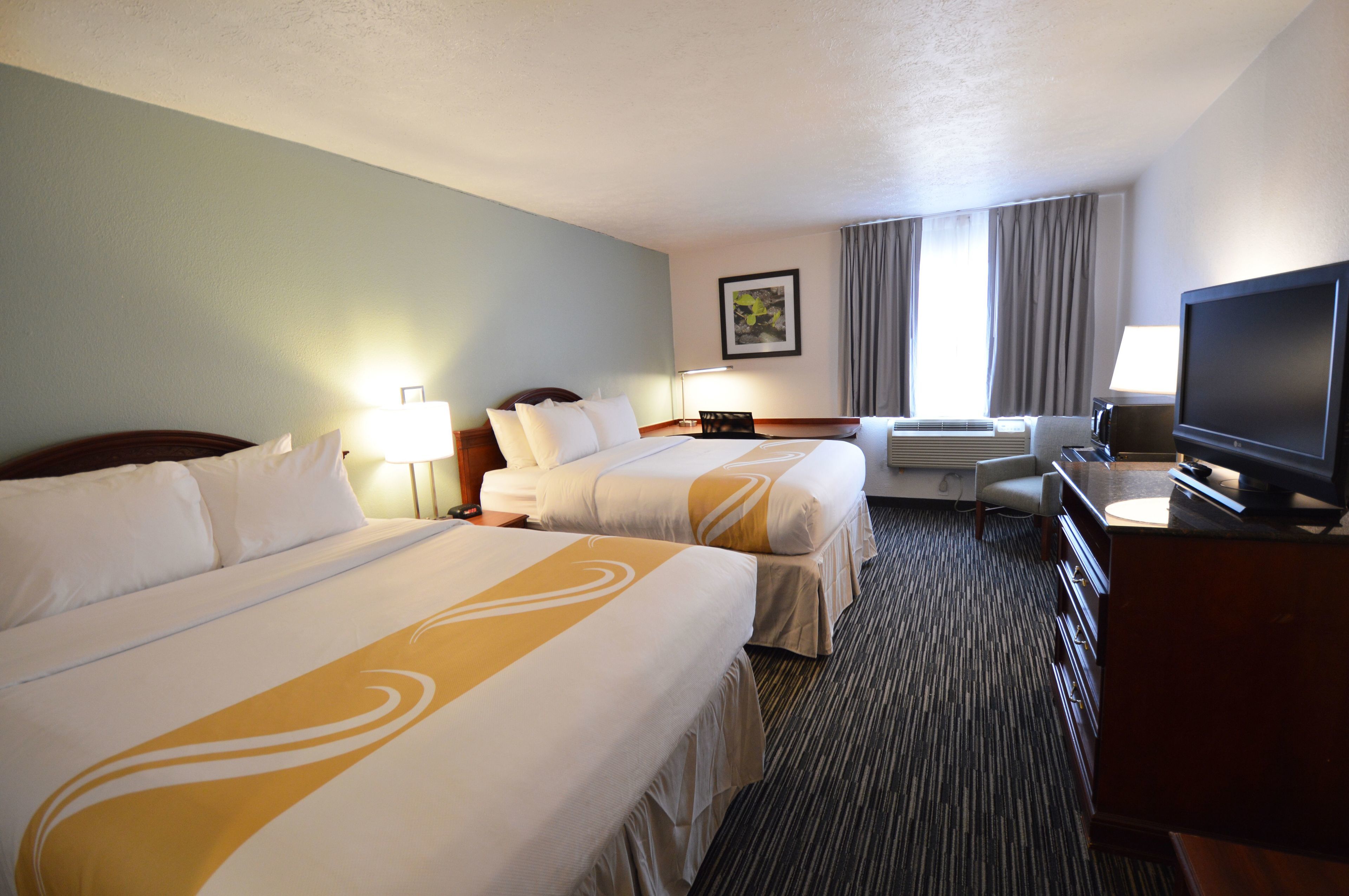 A hotel room with two beds, a television, a desk with a lamp, and a window with curtains.