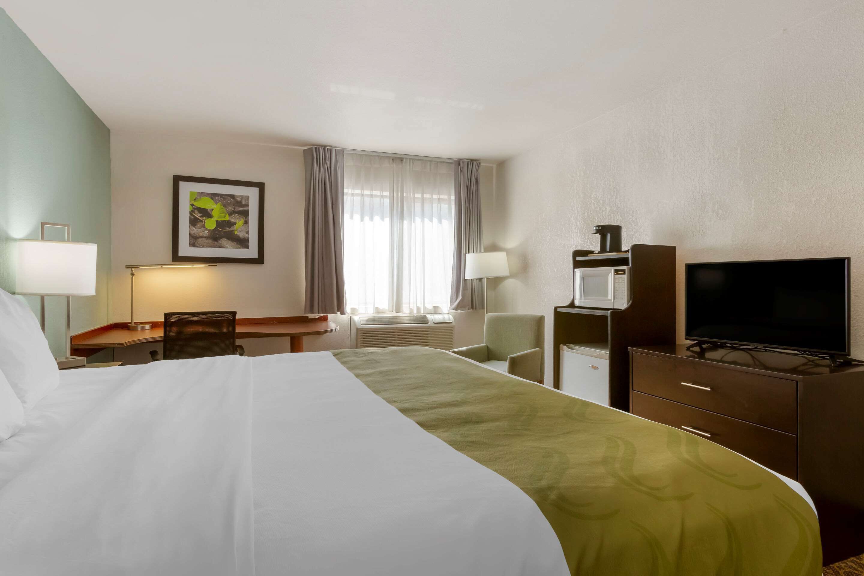 A hotel room with a bed, desk, chair, television, and a window with curtains.