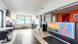 A hotel reception area with a tiled floor, a reception desk, a television, and a window providing a view of the outdoors.