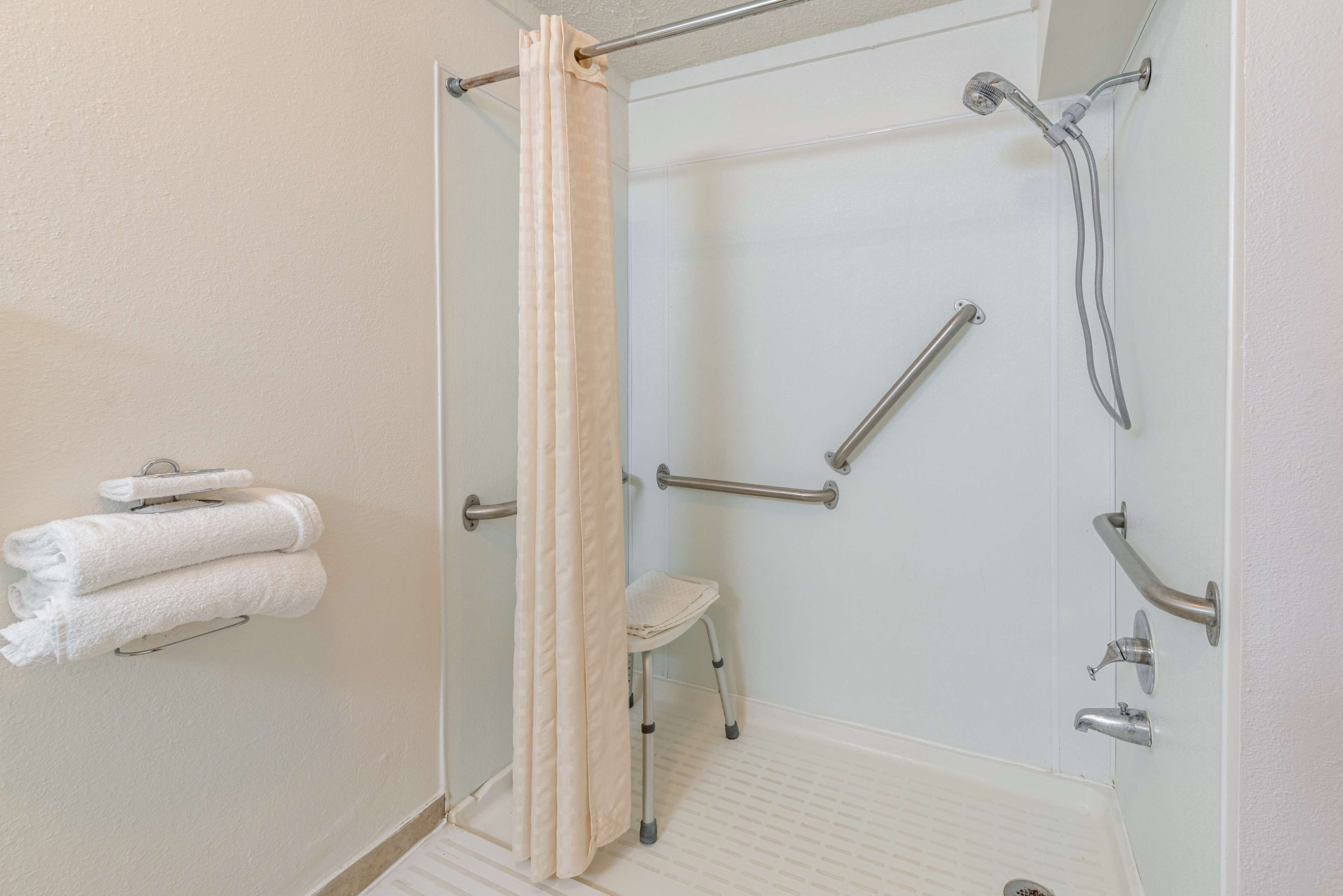 A bathroom with a shower, grab bars, a step stool, and towels on a rack.