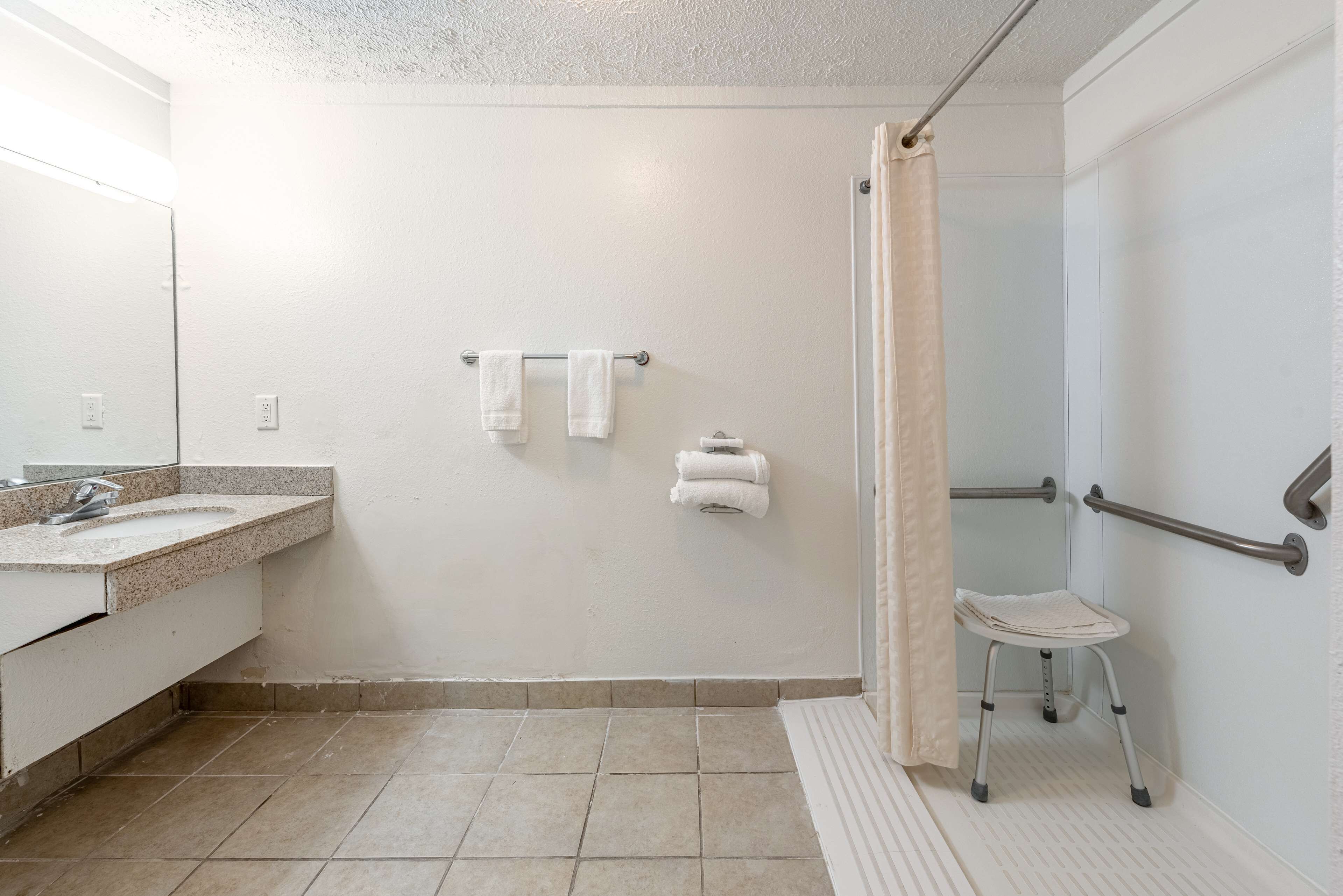 Un baño con lavabo, toallero y ducha con barra de apoyo y taburete.