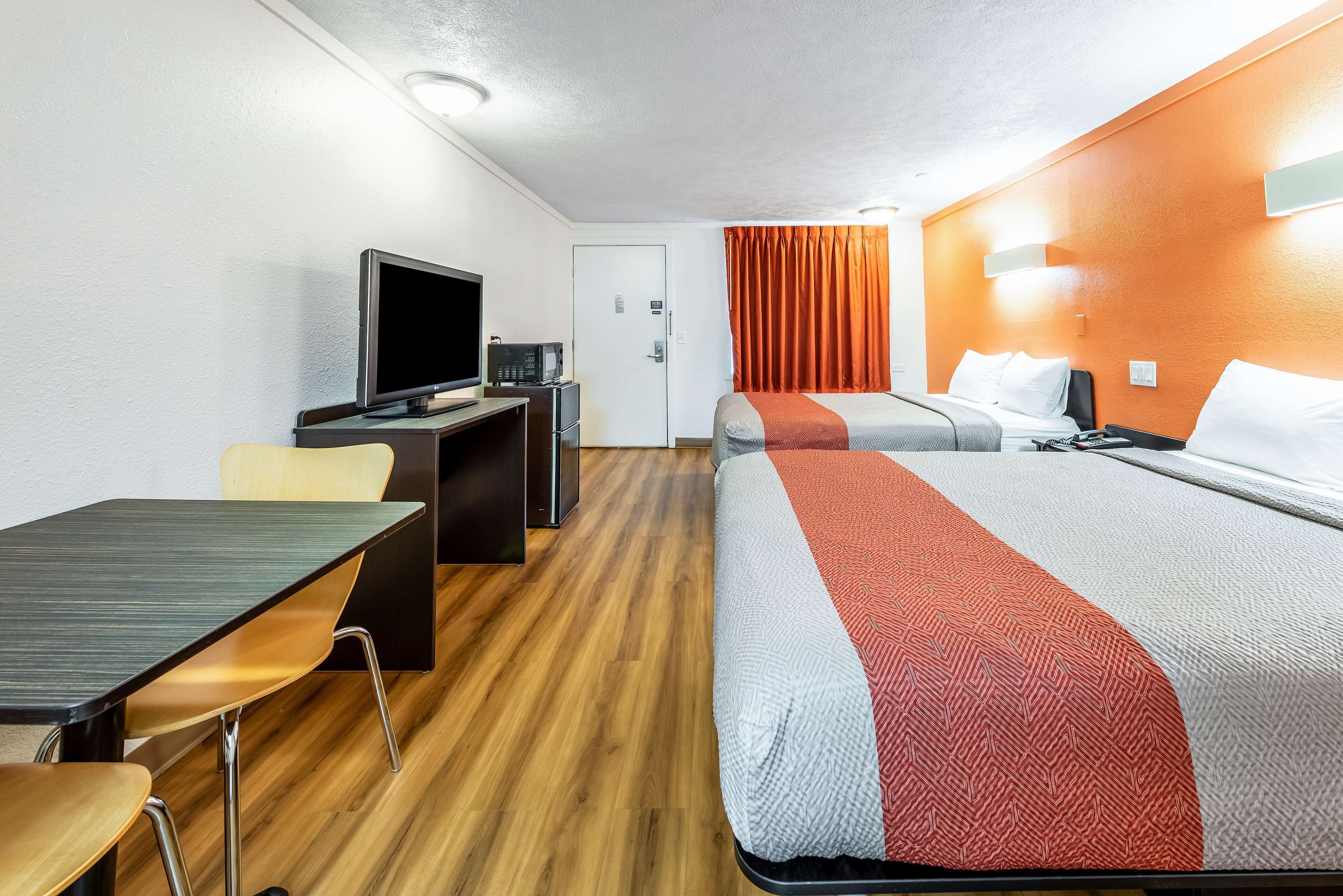 Una habitación de hotel con una cama, un escritorio con televisor, una silla y una puerta.