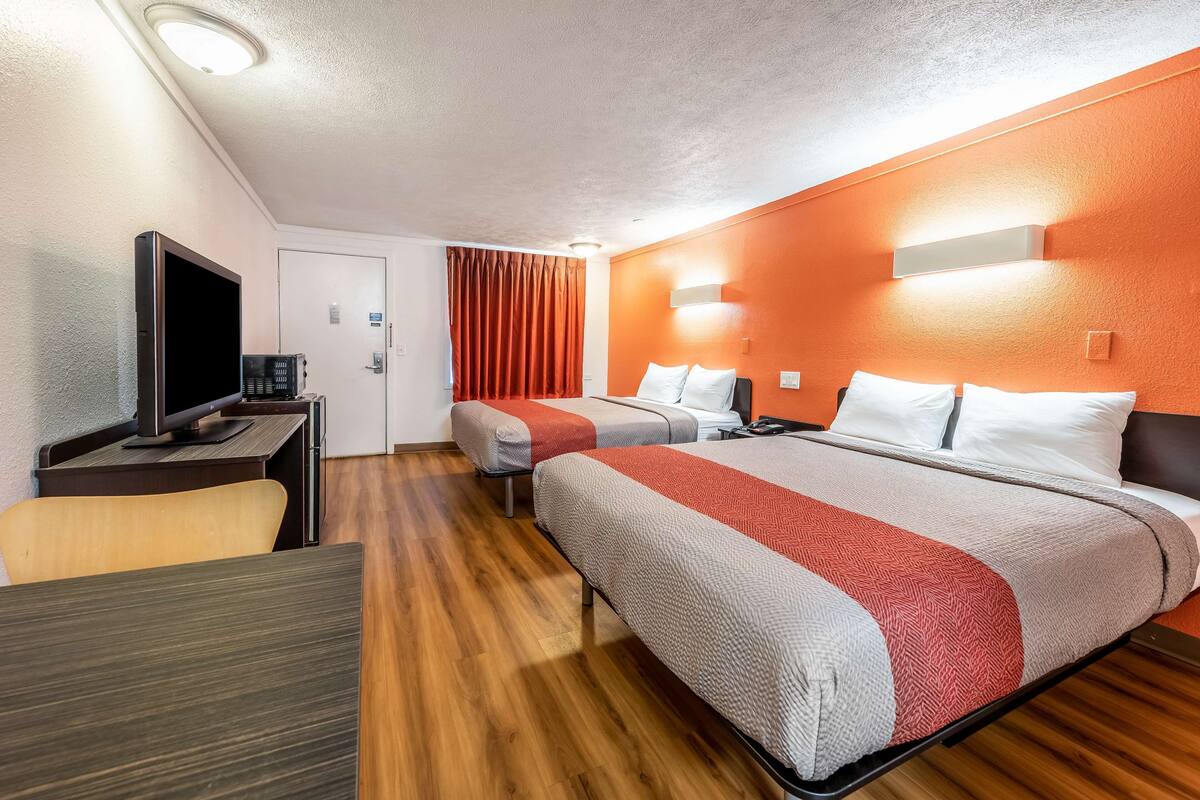 A hotel room with two beds, a desk with a TV, and a wooden floor.