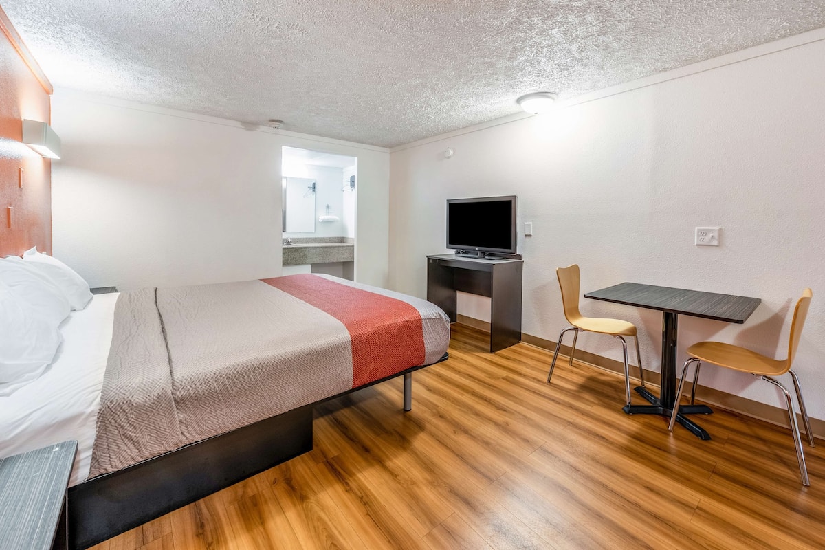 A hotel room with a bed, a desk with a TV, and two chairs.