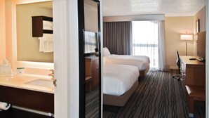 Une chambre d’hôtel avec un grand miroir, un lit, un bureau, une chaise et une fenêtre avec des rideaux.