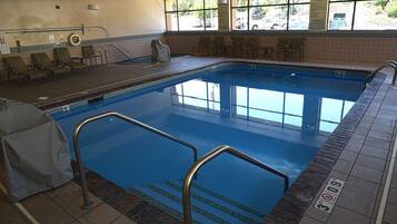 An indoor swimming pool with clear blue water, tiled steps leading into the pool, and several lounge chairs around the pool area.