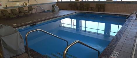 An indoor swimming pool with clear blue water, tiled steps leading into the pool, and several lounge chairs around the pool area.