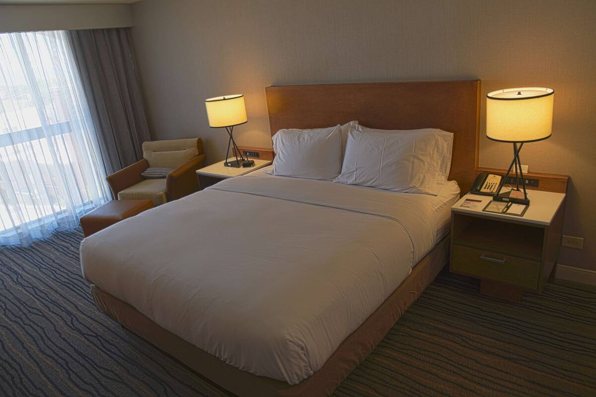 A hotel room with a large bed, two bedside tables with lamps, a chair, and a window with curtains.
