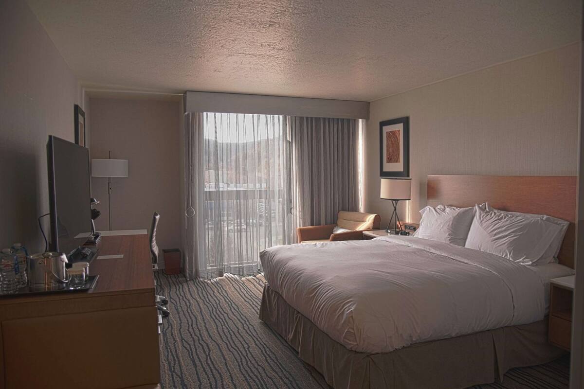 A hotel room with a large bed, a desk with a lamp, a chair, and a television.