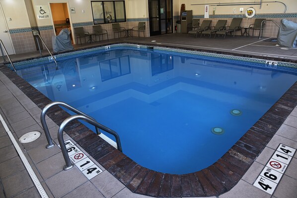 A rectangular indoor pool with a blue tiled edge, a pool lift, and a lifeguard chair.