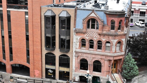 Un immeuble à plusieurs étages, dont la façade est un mélange de briques et de pierres, doté de grandes fenêtres et d’un escalier menant à un niveau supérieur.