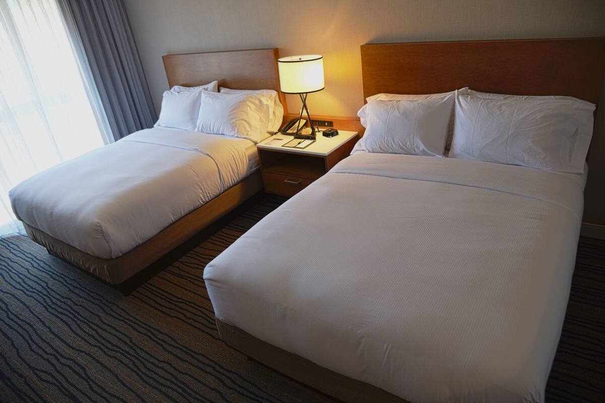 A hotel room with two beds, a nightstand with a lamp, and a window with curtains.