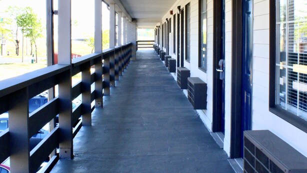 A covered walkway with a metal railing, columns, and a row of doors on one side. - Motel 6 - Dayton, OH (Dayton)