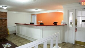 A reception area with a white counter, a red accent wall, a brick fireplace, and a door marked "EXIT". - Motel 6 - Dayton, OH (Dayton)