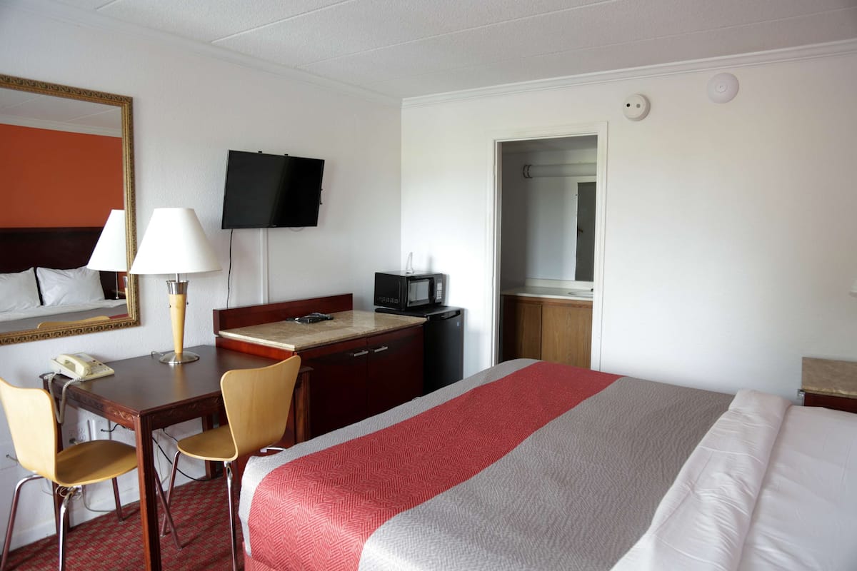 Una habitación de hotel con una cama, un escritorio con teléfono, una silla, un televisor y un microondas.
