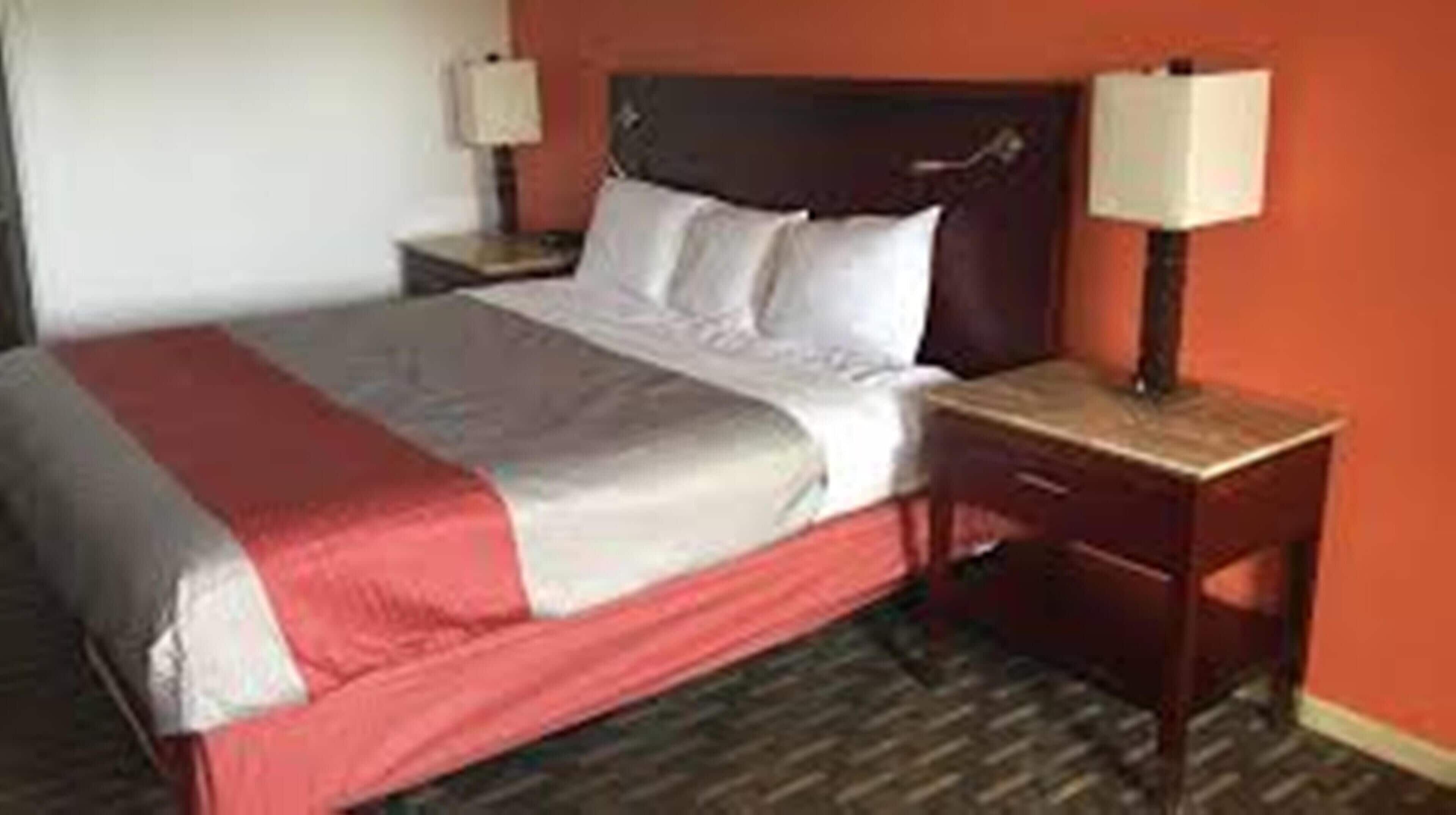 A hotel room with a bed, a nightstand, and a lamp.