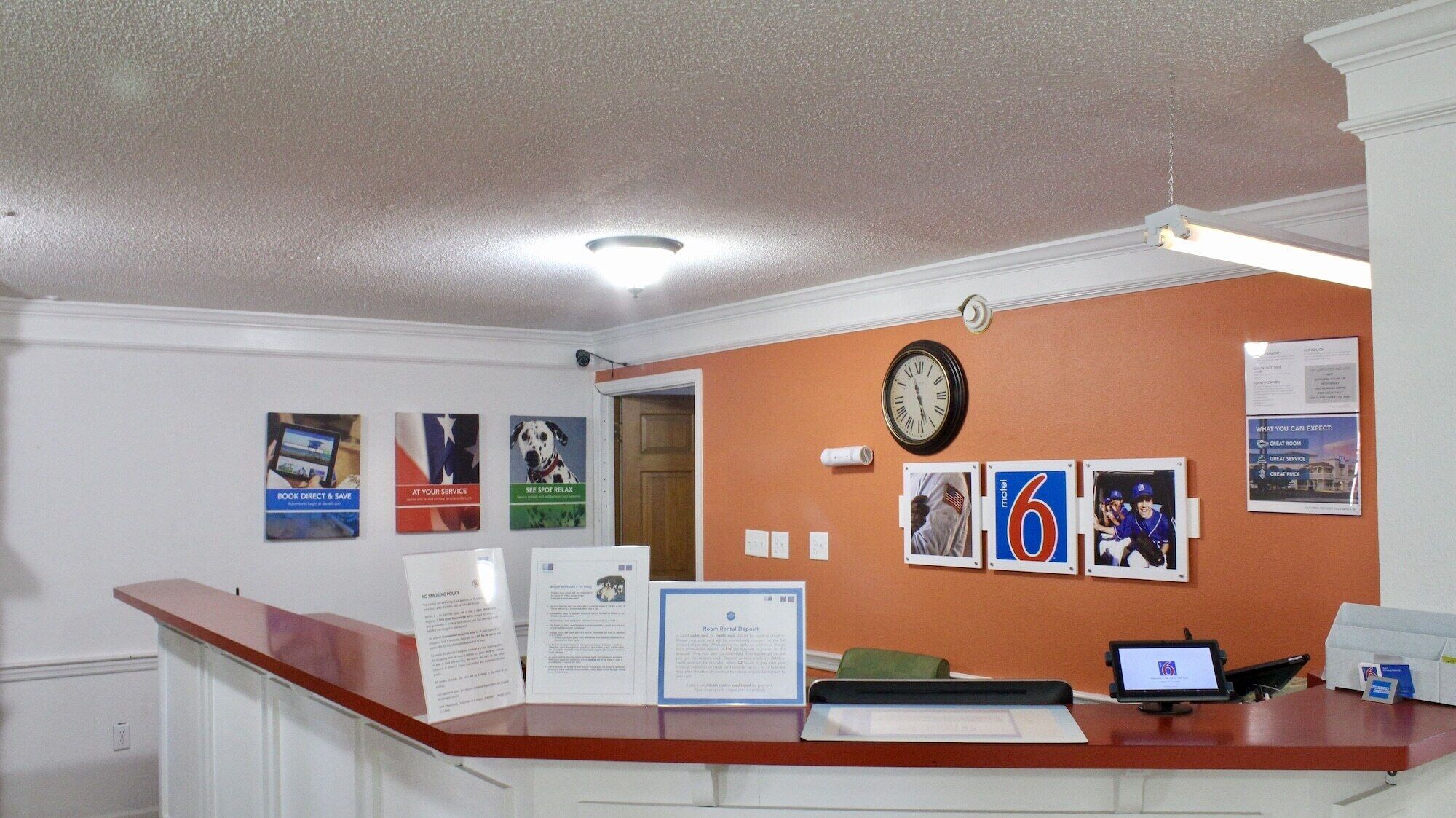 Un espace d’accueil d’hôtel comprenant un comptoir, une horloge et des affiches d’information accrochées au mur.