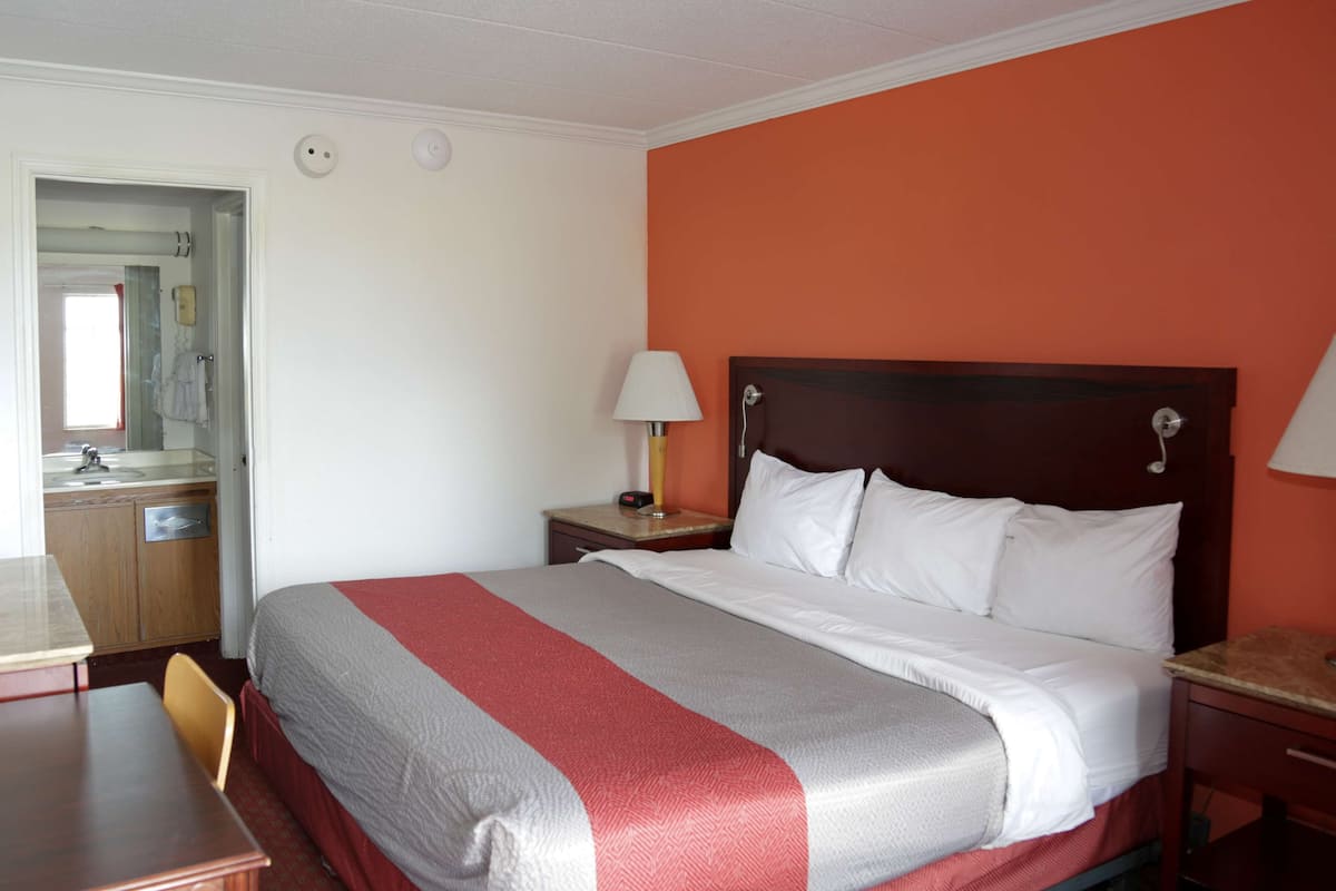 Una habitación de hotel con cama, escritorio y baño visible a través de una puerta abierta.
