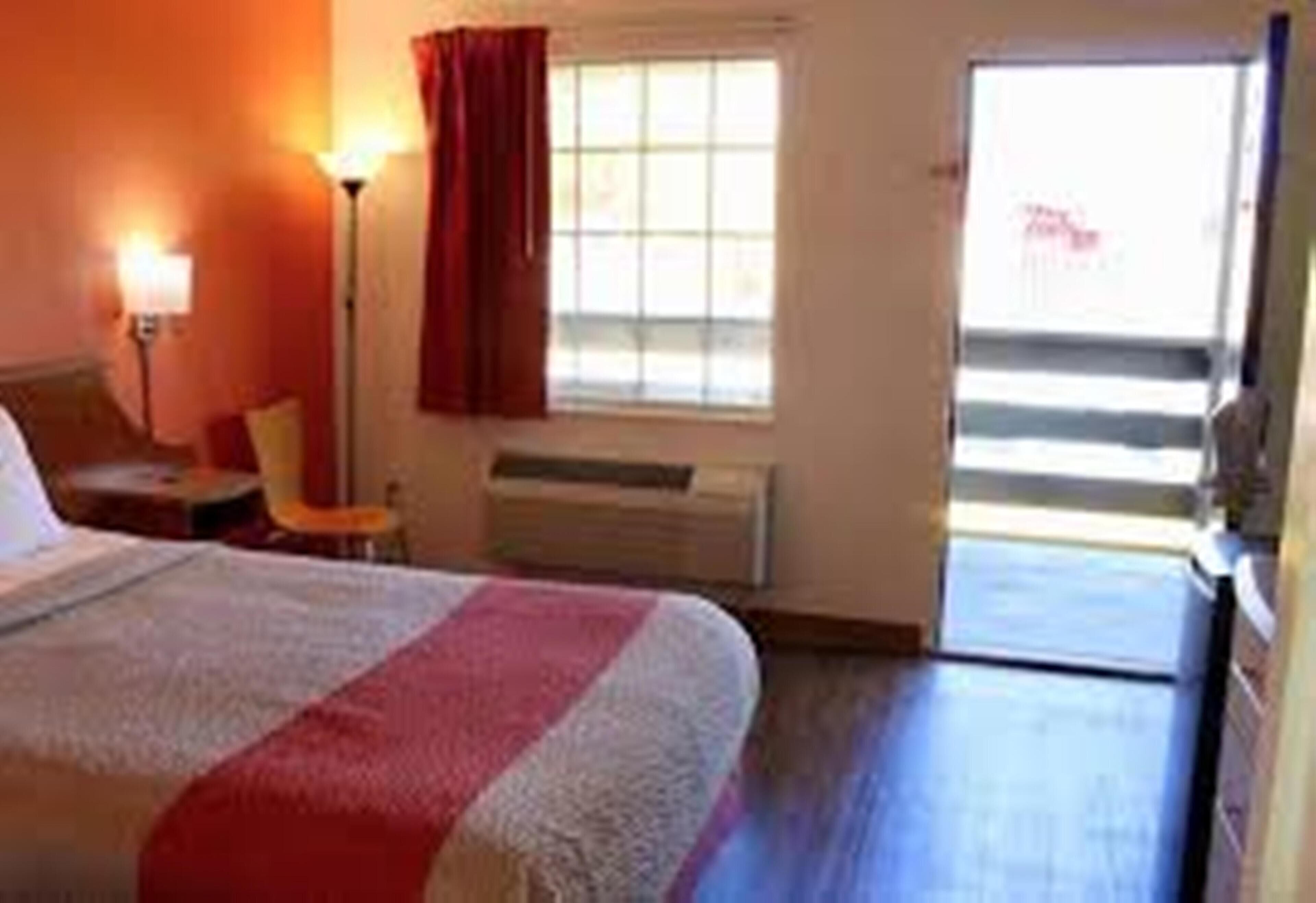 Habitació d'hotel amb un llit, una finestra amb cortines, un radiador i una porta que dona a una zona exterior.