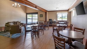 A hotel lobby with a sofa, dining tables, chairs, a TV, and a large window. - Quality Inn Meadville (Meadville)