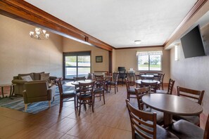 Um hall de hotel com um sofá, mesas de jantar, cadeiras, uma TV e uma janela grande.