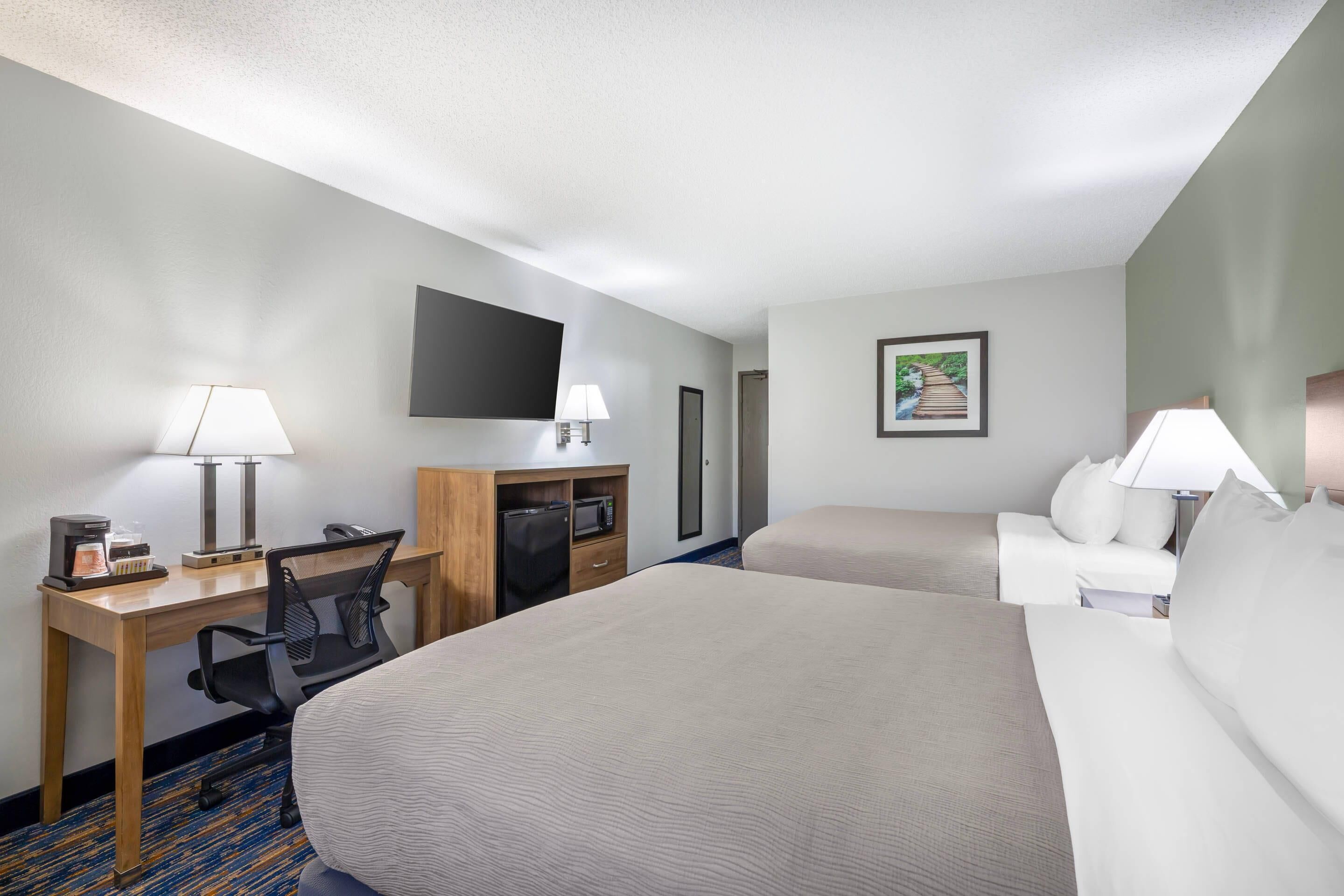 Une chambre d’hôtel avec un grand lit, un bureau avec un ordinateur, une chaise, une télévision et une petite table avec une lampe.