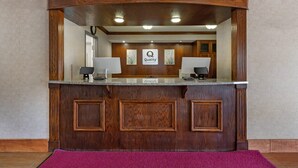 A reception desk with a wooden finish, two lamps, and a sign that reads 'Quality.' - Quality Inn Meadville (Meadville)