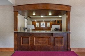 A reception desk with a wooden finish, two lamps, and a sign that reads 'Quality.' - Quality Inn Meadville (Meadville)