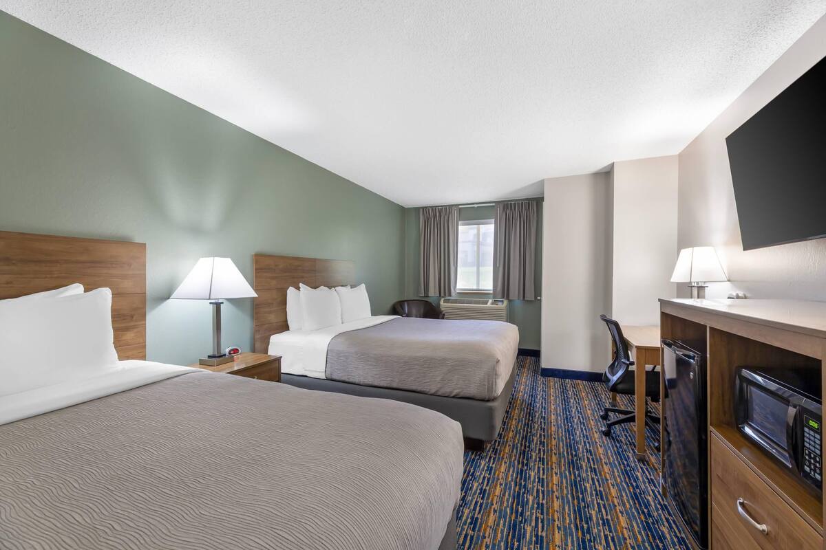 A hotel room with two beds, a desk with a computer, a microwave, and a TV.