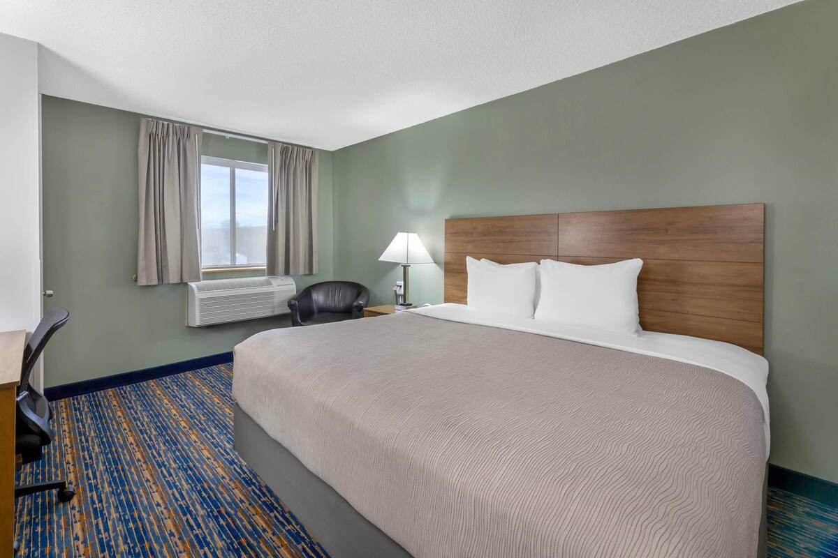 A hotel room with a large bed, a desk, a chair, a lamp, and a window with curtains.