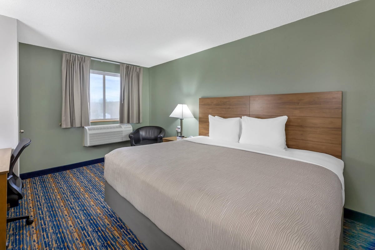 A hotel room with a large bed, a desk, a chair, a lamp, and a window with curtains.