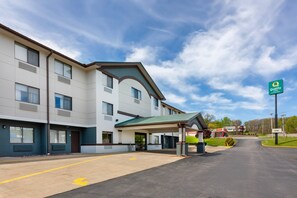A modern hotel with a covered entrance, a parking lot, and a clear sky.