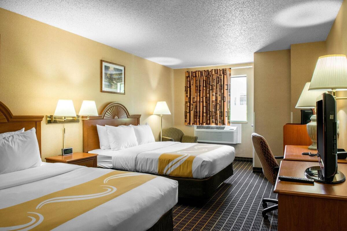 A hotel room with two beds, a desk with a computer, a chair, and a TV.