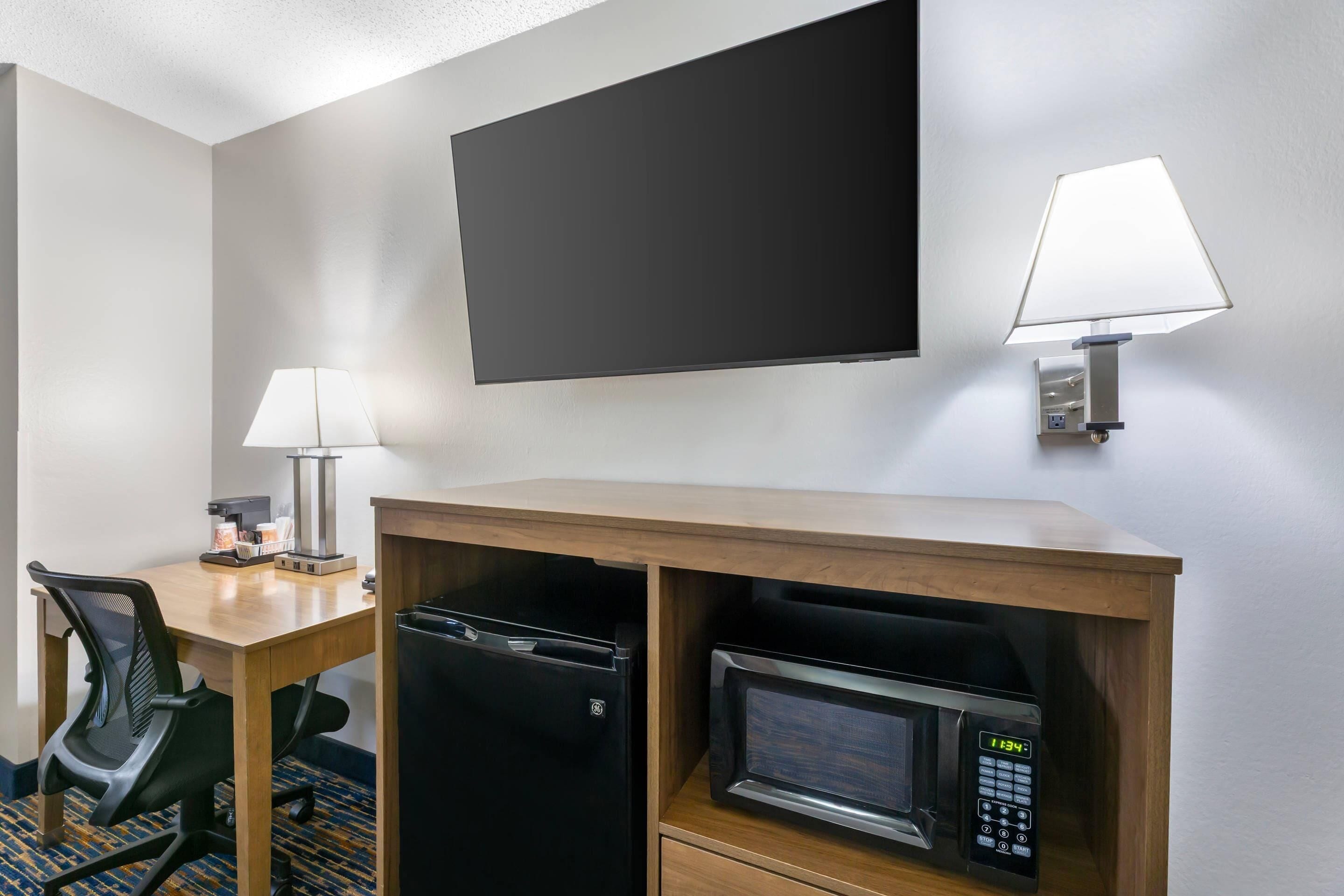 Ein Hotelzimmer mit Schreibtisch, Stuhl, Mikrowelle und einem an der Wand befestigten Fernseher.