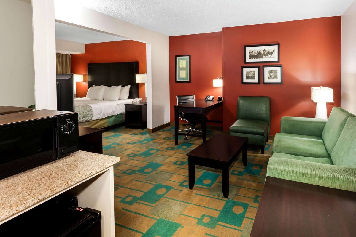 A hotel room with a bed, a desk, a green sofa, a coffee table, and a microwave.