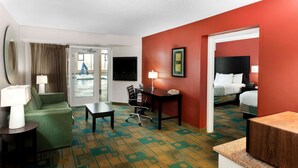 A hotel room with a green sofa, a small table, a desk with a lamp, a bed, and a TV.