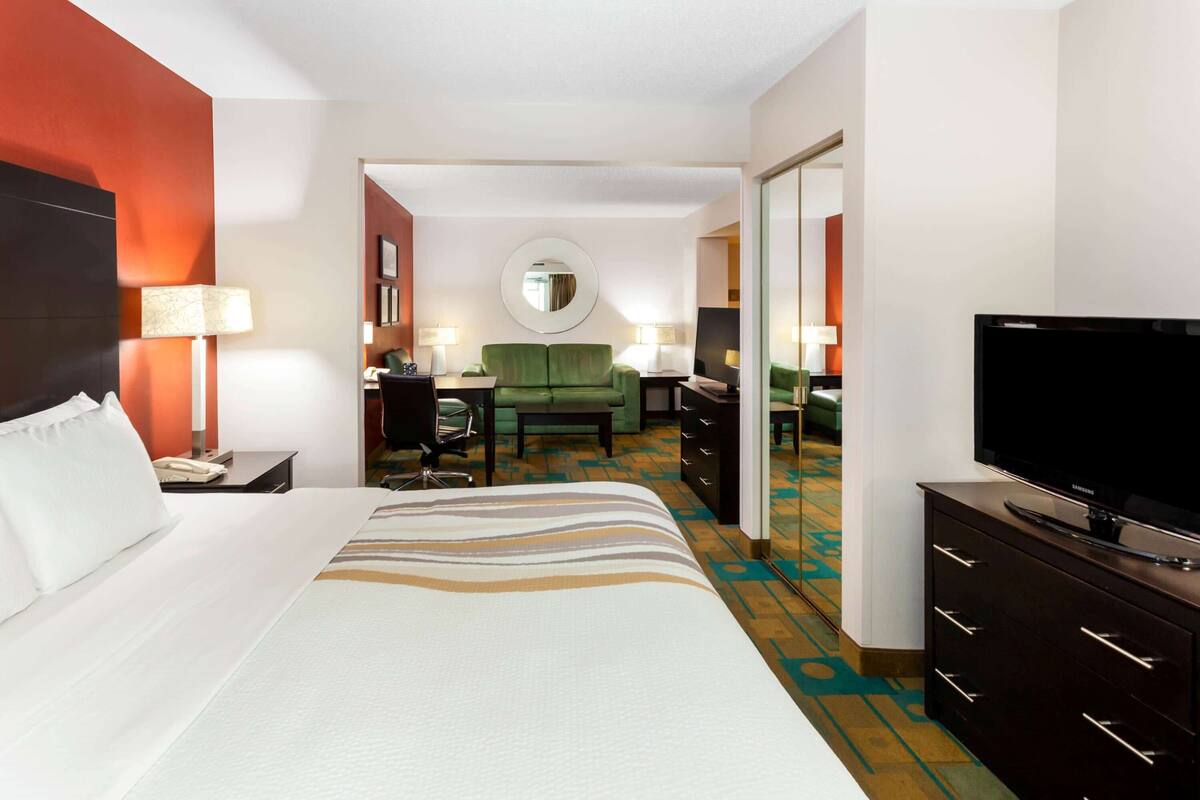 A hotel room with a large bed, a television, a desk with a chair, a green sofa, and a mirror on the wall.