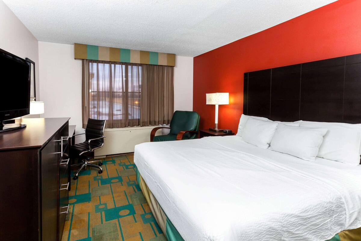 A hotel room with a bed, a desk with a TV, a chair, a lamp, and a window with curtains.