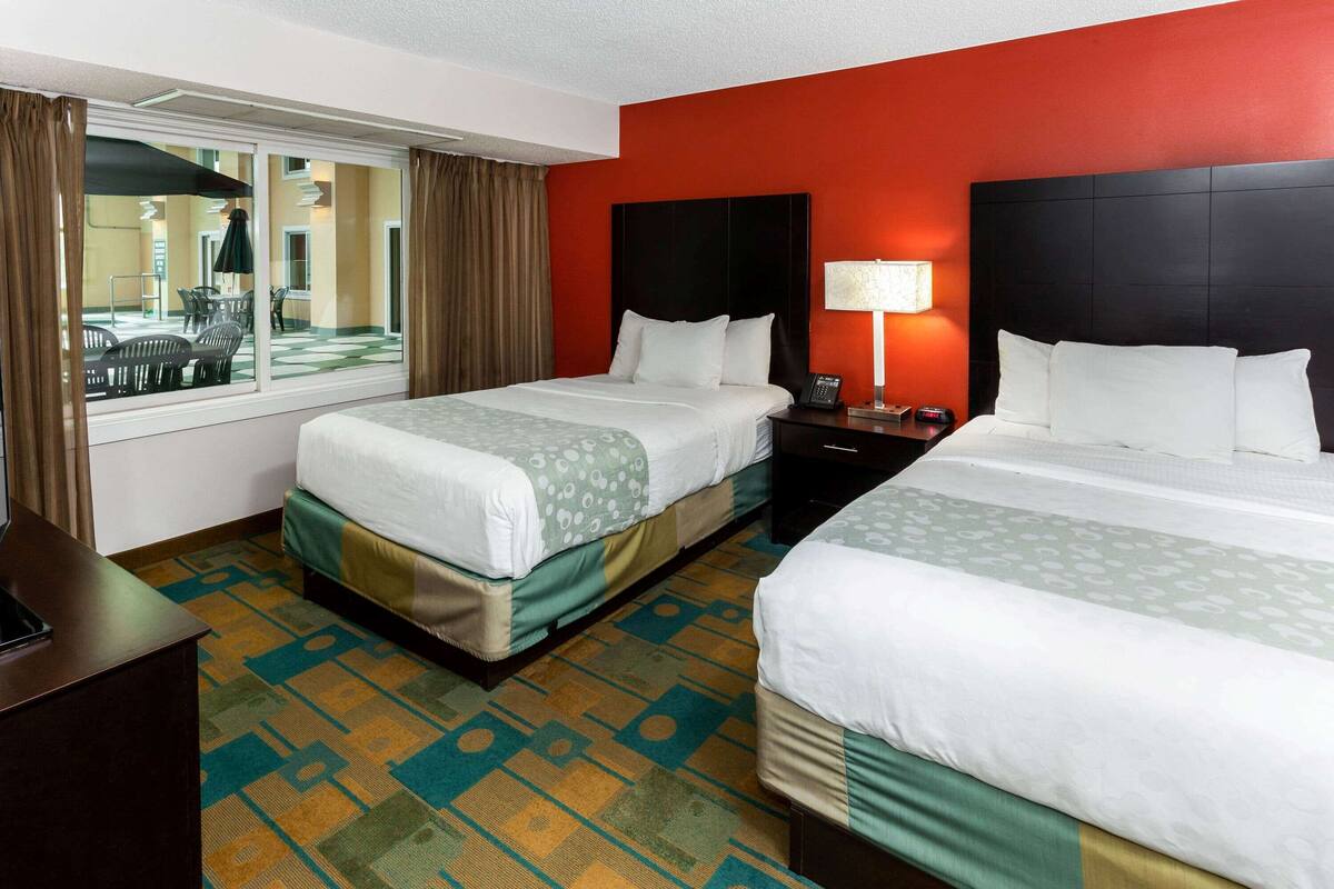 A hotel room with two beds, a window with curtains, a desk, and a patterned carpet.