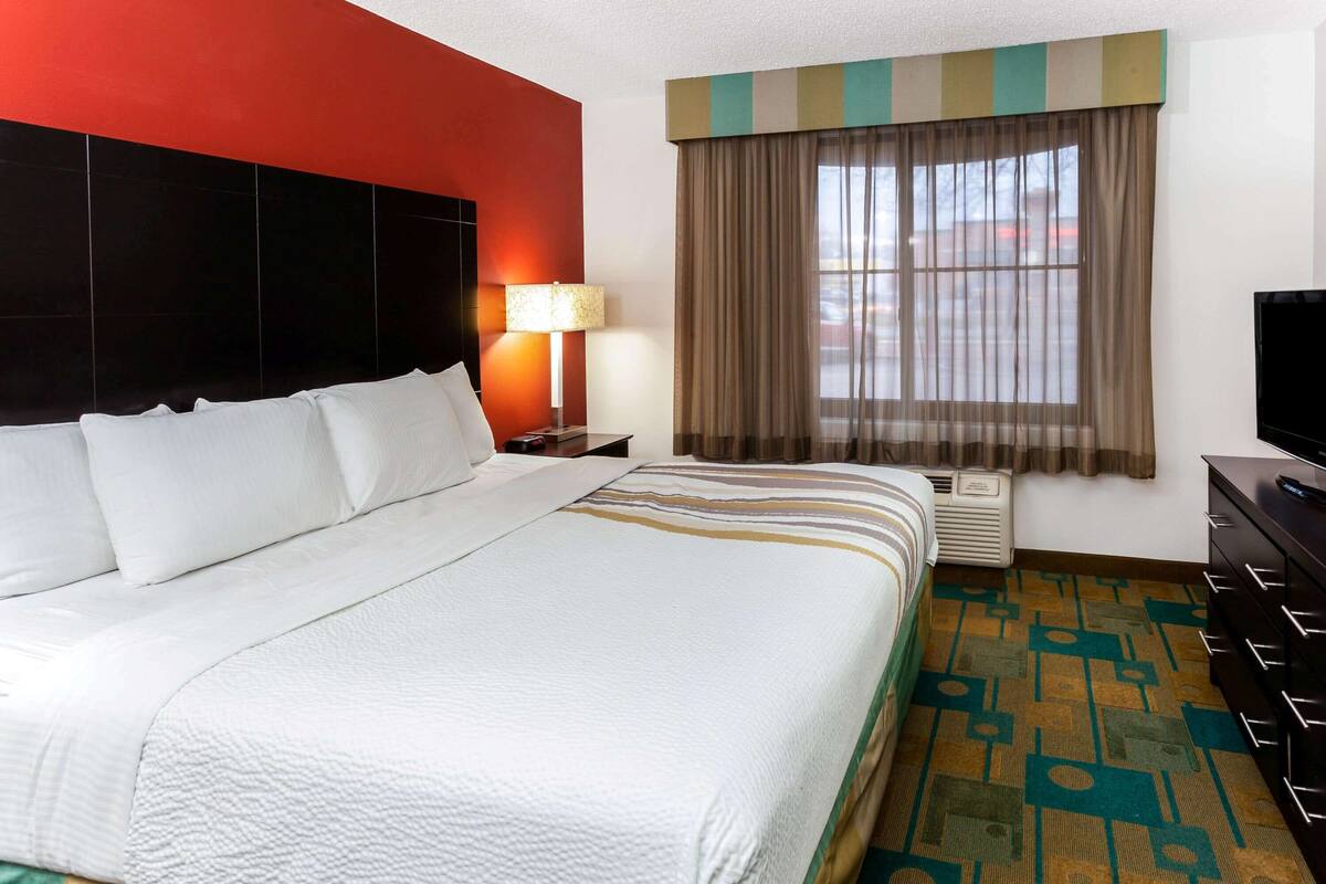 A hotel room with a large bed, a nightstand with a lamp, a television, and a window with curtains.