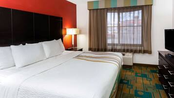 A hotel room with a large bed, a nightstand with a lamp, a television, and a window with curtains.