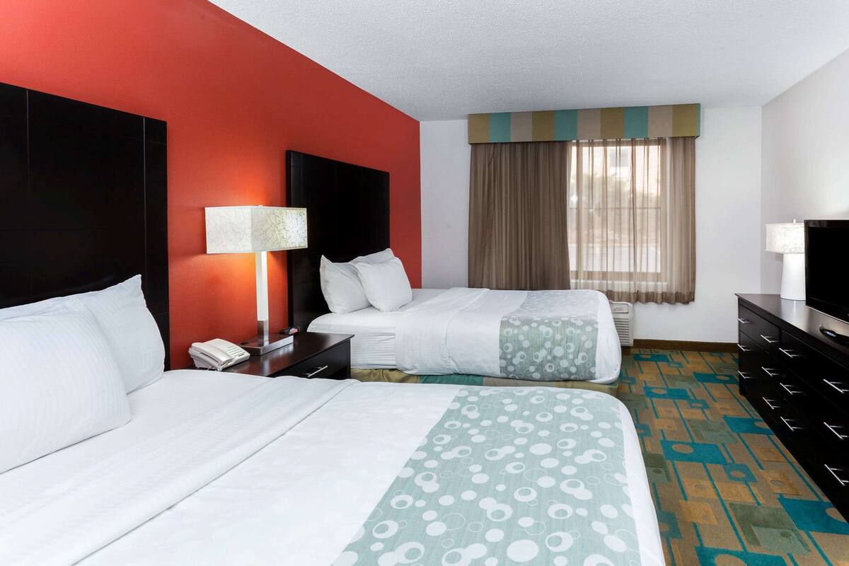 A hotel room with two beds, a desk, a telephone, a television, and a window with curtains.