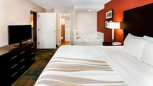 A hotel room with a bed, a television on a dresser, a bathroom with a bathtub, and a nightstand with a lamp.