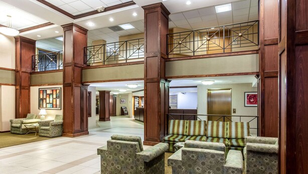 A spacious lobby with a high ceiling, wooden columns, a staircase, and seating areas.