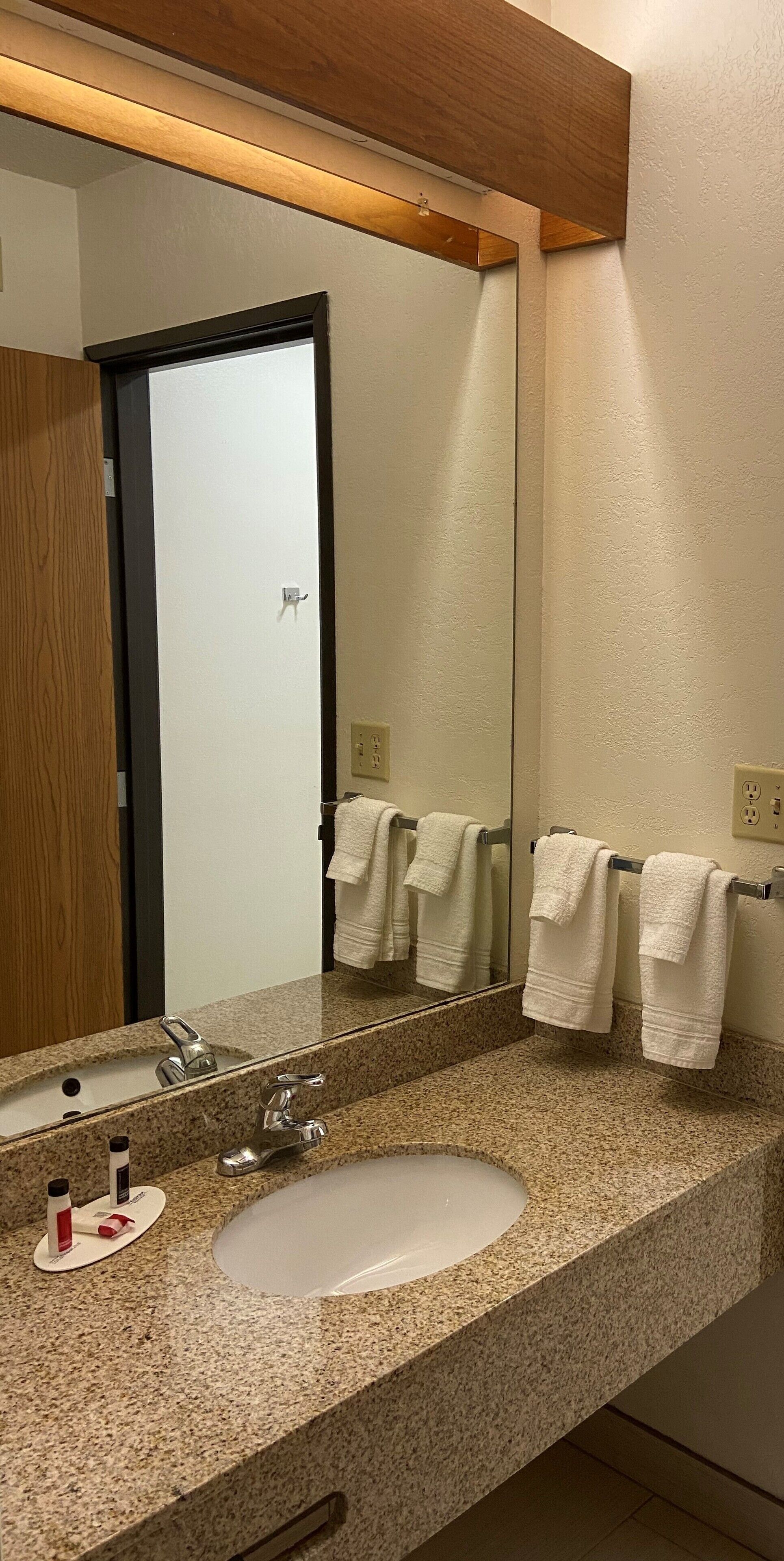 A bathroom with a granite countertop, a sink, a mirror, and two towels hanging on a towel rack.