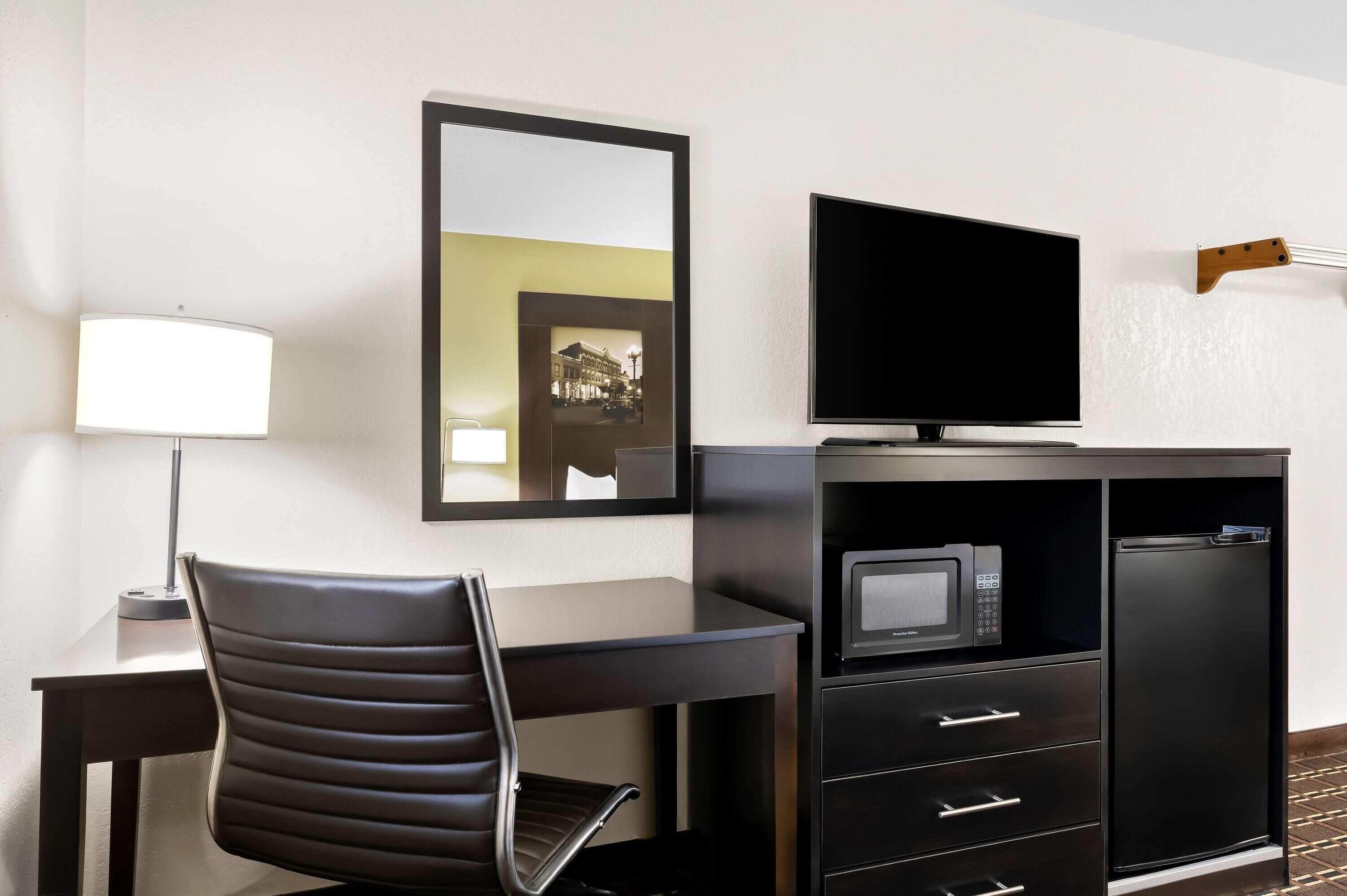 Una habitación de hotel con escritorio, silla, televisor, microondas y un armario.